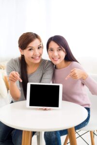 Duas mulheres diante de uma mesa apontando para um tablet