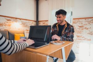 Homem sorridente sentado sobre a mesa com um notebook