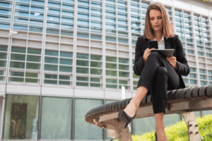 Mulher com trajes formais sentada na calçada usando um tablet corporativo